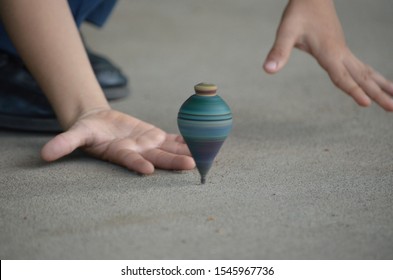 Top View Of A Boy's Hands Trying To Catch A Spinning Top While Spinning At High Speed. Horizontal Image