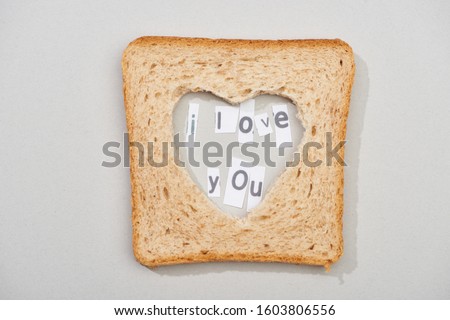 Top view of bread slice with carved heart shape and i love you lettering on grey background