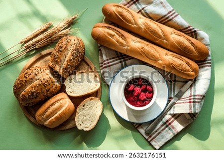 top view of breads as sliced seeded brown cob and baguette ones with bowl of raspberry jam