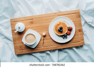 top view of breakfast in bed with tasty pancakes and coffee on wooden tray