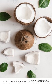 Top view of broken coconut with green leaves on white stone background
