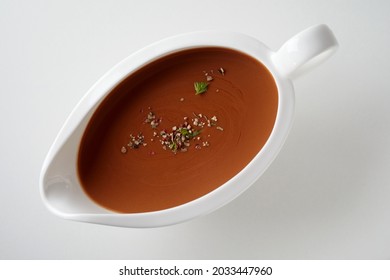 Top view of brown sauce with herbs and spices in ceramic gravy boat place on white surface