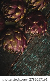 Top view of a bunch of five raw purple artichokes with stems arranged on a dark rustic wooden table with peeling teal paint. Organic Mediterranean food composition.