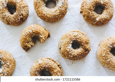 Top view of a bunch of vegan donuts made of almond flour, banana, cinnamon and coconut flakes, with one of them bitten, with white background