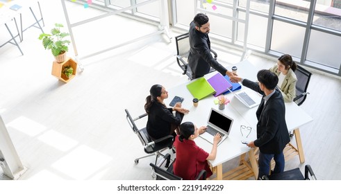 Top View Of Business Partners Shaking Hands Over The Table After Concluding A Business Agreement In Meeting Room With The Team. Business To Succeed Concept.