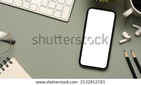 Top view of business table work with keyboard computer, eyeglasses, notepad, pencils earbuds and smartphone white screen mockup on grey background.