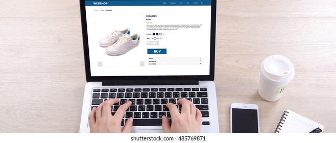 Top View Business Woman Buying Sneakers On Ecommerce Website With Smart Phone And Coffee On Wooden Desk