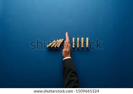 Top view  of businessman hand stopping falling dominos in a business crisis management conceptual image.