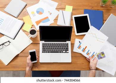 Top View Of The Businessman Using Mobile Phone And Working With Laptop By Messy Desk. Empty Screen For Copy Space, Top View. Overworking Concept