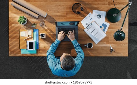 Top View Of Businessman Working On Computer At Desk With Paperwork In Home Office.