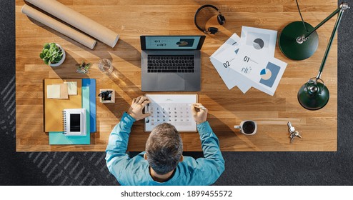 Top View Of Businessman Working On Computer At Desk With Paperwork In Home Office.