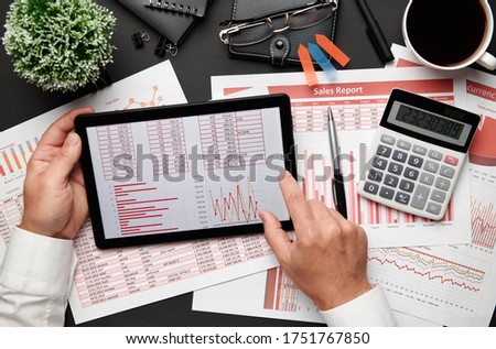 Top view of businessman's hands working with tablet pc and financial reports. Modern black office desk with notebook, pencil and a lot of things. Flat lay table layout.