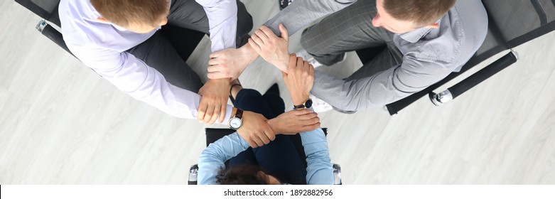 Top View Of Businesspeople Putting Hands Together In Office. Good Deal. Support And Team Work. Employees Sitting On Chairs In Stylish Suits. Business And Career Success Concept