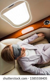 Top View Of Businesswoman With Sleeping Mask Sitting Near Airplane Window In Private Plane 