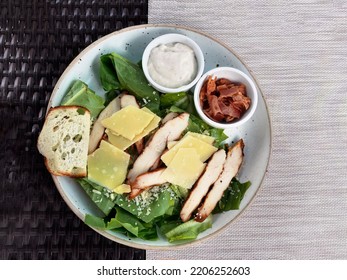 Top View Caesar Salad, Chopped Cos Lettuce, Sliced Of Grilled Chicken Breast, Grated Parmesan Cheese And Hard Cheese, Serving With Ciabatta And Small Bowl Of Sauce And Croutons, In The Ceramic Plate