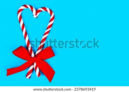Top view candy cane striped in Christmas colors in shape of a heart with red bow on blue background. Closeup. Christmas, holidays season. copy space.