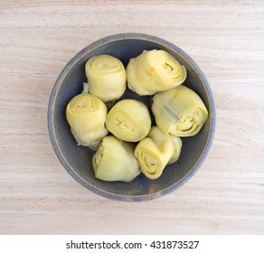Top view of canned artichoke hearts in an old bowl on a wood table top.