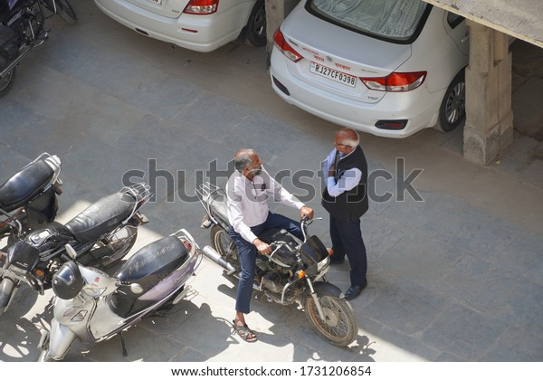 Top view of car and\
bike parking in India. Bike, scooters and Cars parking under in\
shadow in summer season at City. Two people are talking.: Udaipur\
India - May 2020