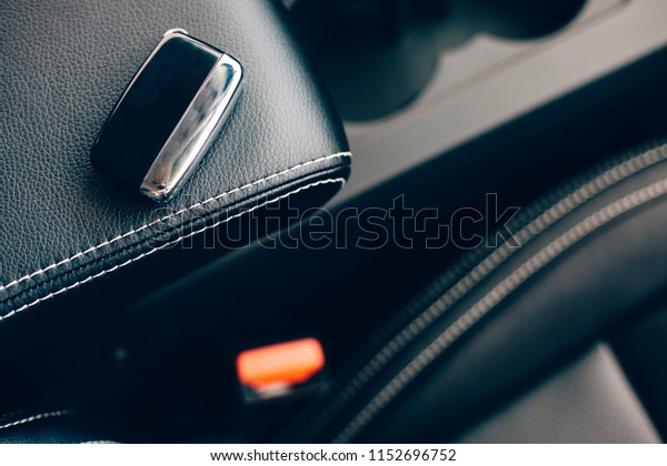 Top view\
of a car key placed on a front armrest in handmade black leather\
upholstery of an elegant car. Top\
view