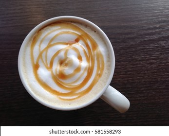 Top View Of Caramel Latte In Coffee Cup On Dark Wooden Table