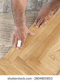 Top view of carpenter hands installing herringbone parquet planks on adhesive base during apartment renovation, hardwood floor construction, residential remodeling and interior finishing
