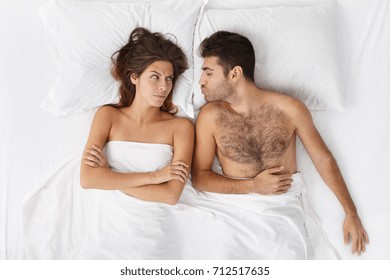 Top View Of Caucasian Family In Bed Before Sleep: Handsome Sleepy Man With Bristle Kissing Good Night His Beautiful Annoyed Female With Arms Folded Who Is Mad At Him Because He Came Home Drunk Again