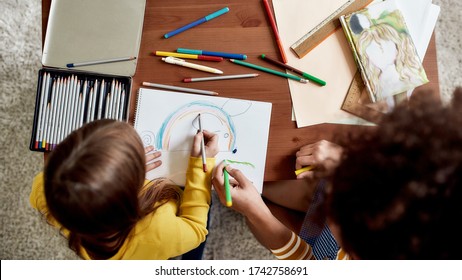 Top view of caucasian little girl spending time with african american baby sitter. They are drawing a mouse together. Children education, leisure activities, babysitting concept. Selective focus