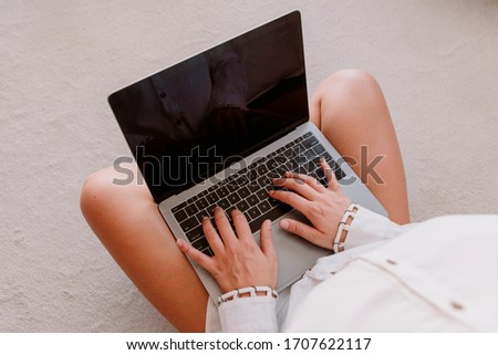 Top view of caucasian young woman with a grey computer sitting on the white and soft floor of the bedroom. foreground. closeup.