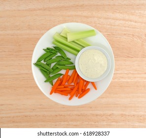 Top View Of Celery, Carrots And Sugar Snap Peas On A Plate With A Bowl Of Ranch Dressing To The Side On A Wood Table.