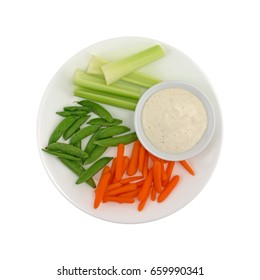 Top View Of Celery, Carrots And Sugar Snap Peas On A Plate With A Bowl Of Ranch Dressing To The Side Isolated On A White Background.