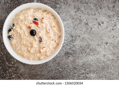 Top View Of Cereal Bowl Filled With Bircher Muesli With Blueberries And Cranberries On Stone Kitchen Counter