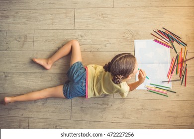 Top View Of Charming Little Girl Drawing Using Colorful Pencils While Lying On The Floor In Her Room At Home