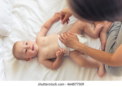Top view of charming naked little baby looking at his mommy and smiling while she is changing him nappies