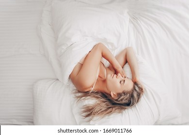 Top view of a charming slim young lady sleeps in bed on white sheets and sees sweet dreams on weekend. Relaxed girl is resting after a long working week. Relaxation Sleep Recovery. Hotel business trip