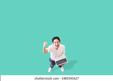 Top View Of Cheerful Asian Man Holding Computer Laptop On Isolated Background Feeling Win ,celebrating And Victory. Young Asian Man Lifestyle Concept Green Background.