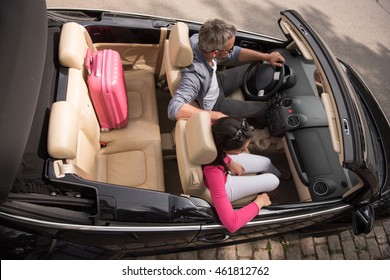 Top view. A cheerful couple going on a road trip in their convertible car, there is luggage on the back seat, the man has grey hair, the woman is brunette