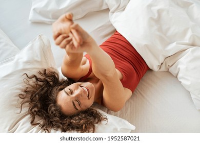 Top view of cheerful woman waking up after sleep and stretching on bed. High angle view of beautiful girl lying on bed and stretching after wake up. Awake woman wake up in morning and feeling fresh. - Powered by Shutterstock