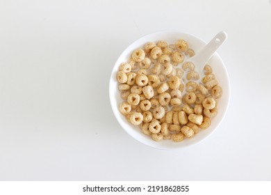 Top View Of Cheerios In Bowl Of Milk With Spook On Right Side Of White Table Background, A Healthy Morning Oat Cereal With Low Sugar And High Fibre For Breakfast, Copy Space On Left