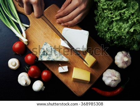 Top view of cheese collection on wooden desk. Close-up of woman hands cutting feta for breakfast. 