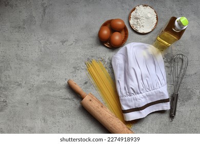 Top view of chef hat with cooking ingredients and utensils on grey rustic background