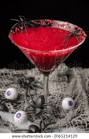 Top view of cherry cocktail for Halloween with spiders, on table with spiders and eyes, selective focus, black background, vertical