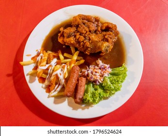 Top View Of Chicken Chop With Sausage, Vegetable And Black Pepper Sauce In Plate Over Red Table.