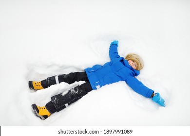 Top View Of Child Doing Snow Angel. Little Boy Playing In Snowdrift And Having Fun With Fresh Snow. Active Outdoors Leisure For Kids On Nature In Snowy Winter Day.