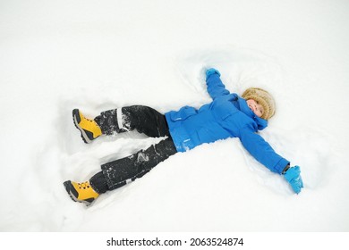 Top View Of Child Doing Snow Angel. Little Boy Playing In Snowdrift And Having Fun With Fresh Snow. Active Outdoors Leisure For Kids On Nature In Snowy Winter Day.