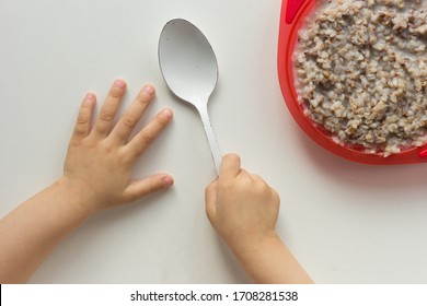 Top View Of Child Hands Holding Spoon In Right Hand And Buckwheat Porridge On White Background