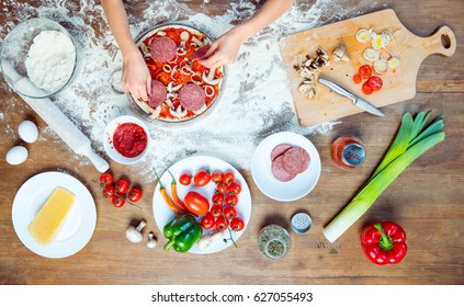 Top View Of Child Making Pizza With Pizza Ingredients, Tomatoes, Salami And Mushrooms On Wooden Tabletop 