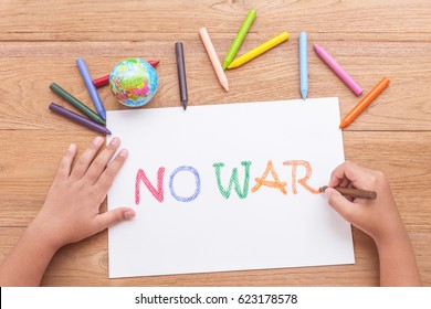 Top view children hand is writing "NO WAR" in white paper with color crayon on brown wooden table - Powered by Shutterstock