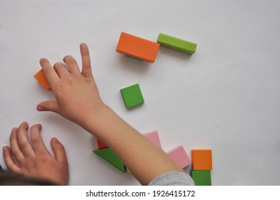 Top View Of Child's Hands Playing With Colorful Wooden Bricks On White Table Background. Boy Building With Wood Constructor. Education Concept