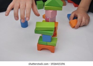 Top View Of Child's Hands Playing With Colorful Wooden Bricks On White Table Background. Boy Building With Wood Constructor. Education Concept