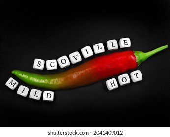 top view of a chilli with different degrees of ripeness on black background, from mild green to hot red, scoville described with white letter cubes
